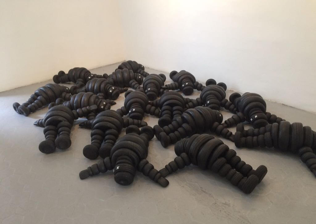 Black sculptural form resembling stacked tires on a white background.